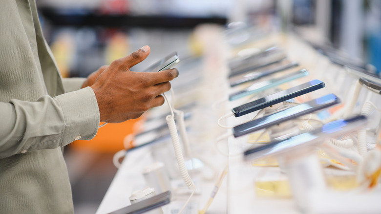 Person testing a smartphone at a store display with several phones lined up.