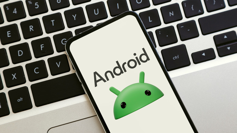 The Android logo seen on a the display of a smartphone placed on top of a laptop.