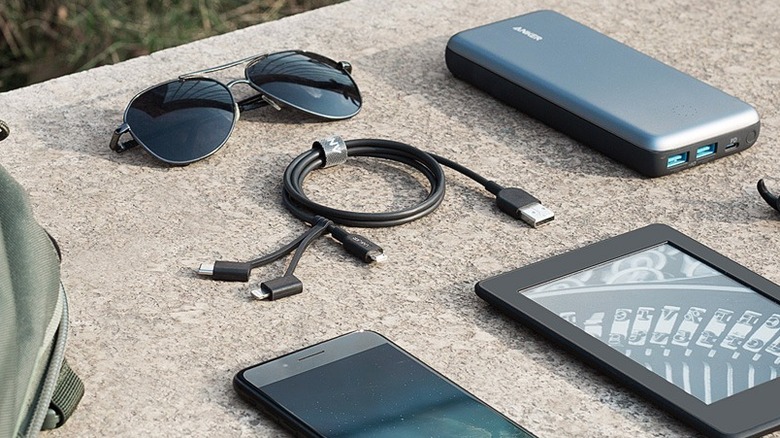 An Anker 321 USB-A to Lightning/USB-C/MicroUSB Cable on a stone surface with multiple electronics