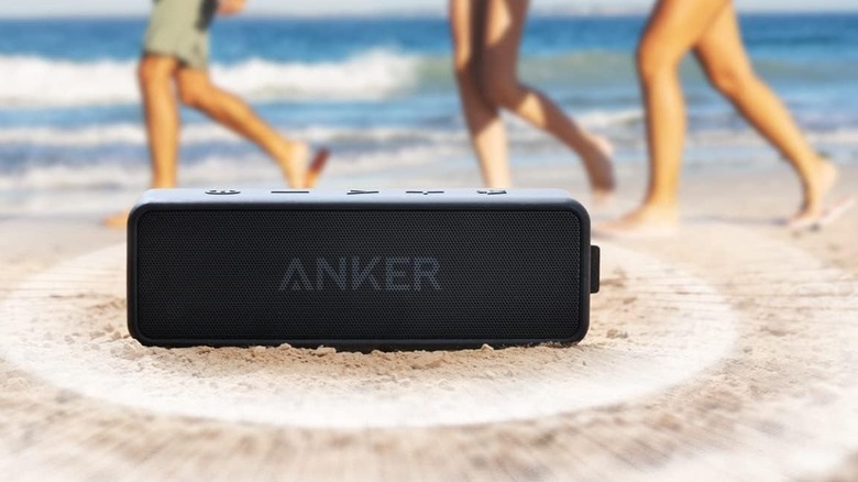close-up Anker Soundcore 2 speaker on the sand, feet of people walking in the background