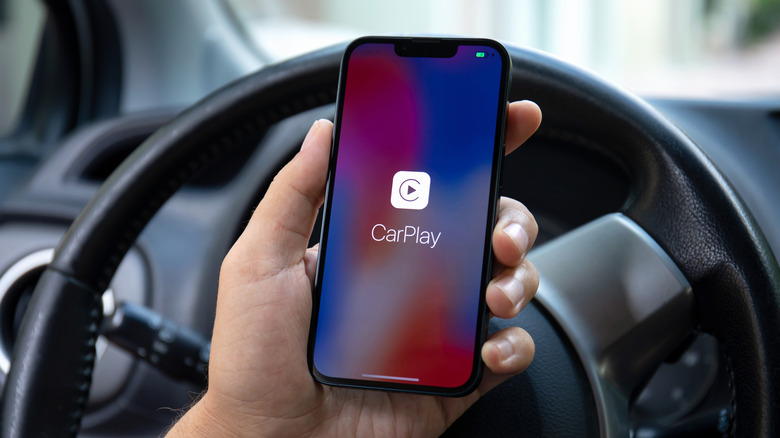 Hand holding an iPhone with the CarPlay logo on the display in a vehicle