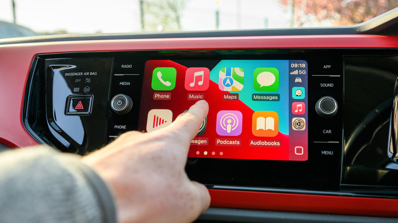 A finger reaching for the Apple Music app on a vehicle display