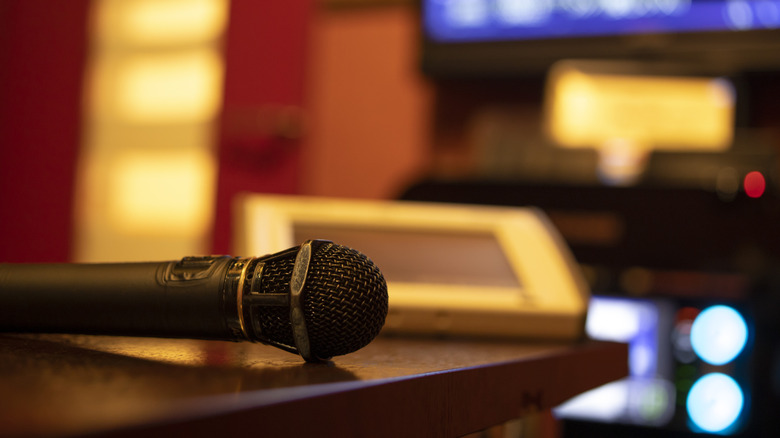 A black microphone sitting on a dark brown table, the background is too blurred to make out the objects present in the image