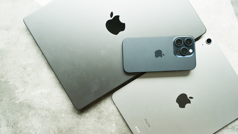 A silver MacBook sits next to a silver iPad Air as a black iPhone sits on top of the two devices