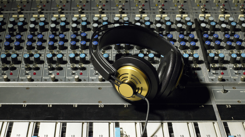 A pair of black and gold headphones sit on top of a silver mixing board that possesses many knobs