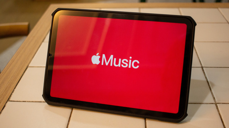 A small black tablet sits on what appears to be the edge of a kitchen counter, the tablet is displaying the Apple Music logo