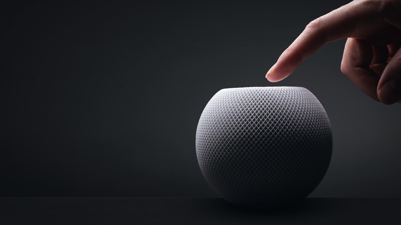 Apple HomePod mini with a hand on dark background