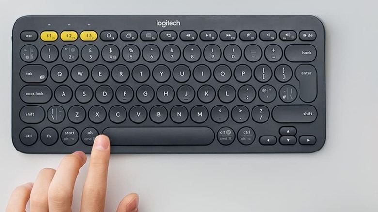 The Logitech K380 Bluetooth Keyboard set up on a table with a hand hovering over it.