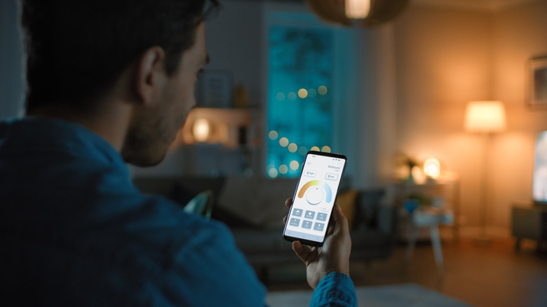 Man looking at an electricity monitoring app on a phone with lights on in the background