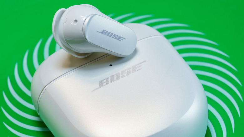 The Bose QuietComfort Ultra Earbuds and charging case placed against a green backdrop.