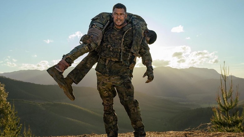Still of Alan Ritchson as 81 from the movie War Machine carrying his brother.