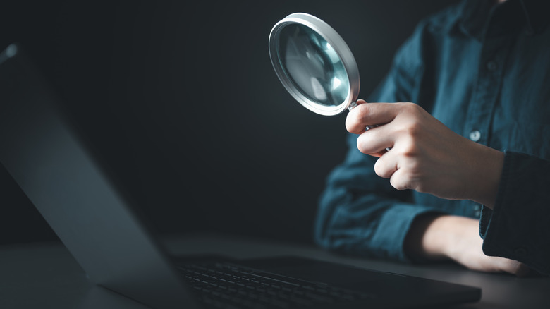 Magnifying glass held in hand and pointed at laptop screen