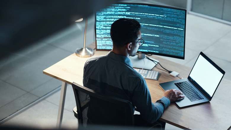 A man using a computer monitor and laptop.