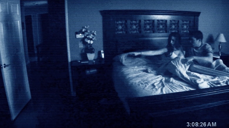 Katie and Micah in bed pointing at a shadow on a door in Paranormal Activity