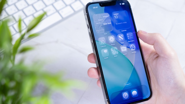 Hand holding iPhone with iOS 26 home screen