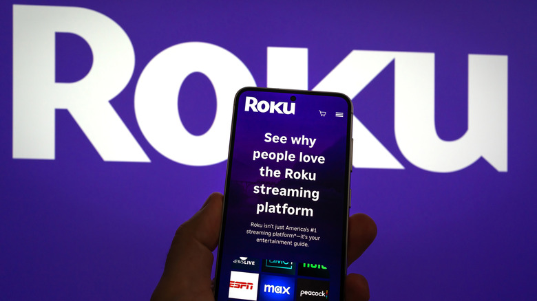 The Roku website on a phone in front of the Roku logo.