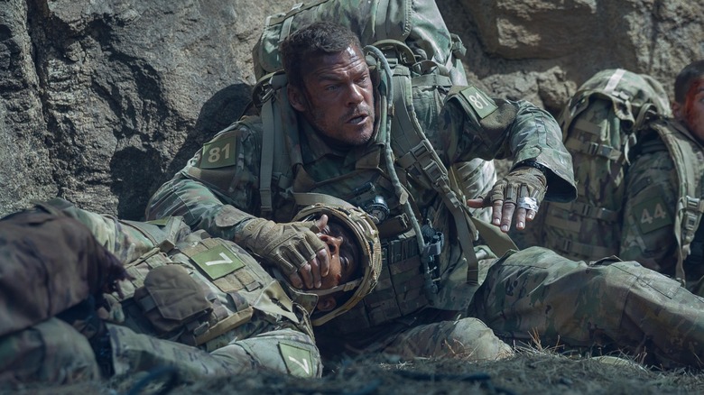 Alan Ritchson covering a soldiers mouth looking scared in War Machine