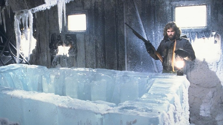 Kurt Russell in The Thing holding a light and a gun inside a frozen room