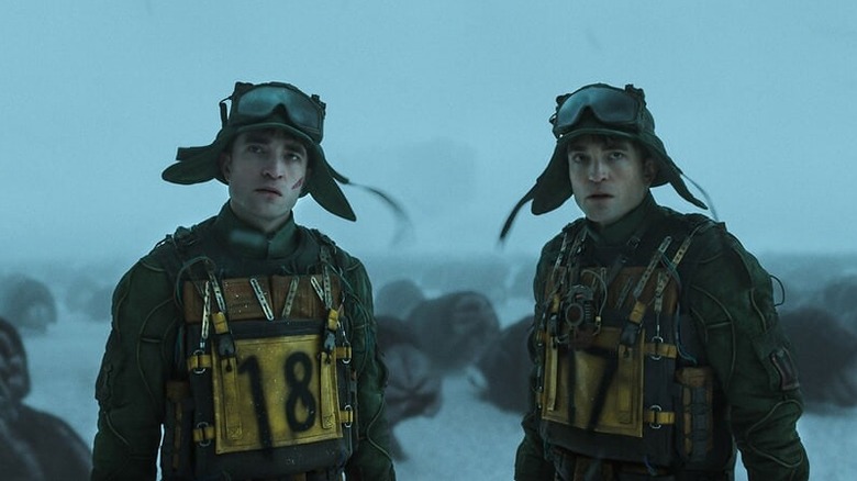 Two Robert Pattinson clones stand side-by-side wearing futuristic army fatigues, starring off in the distance as a pack of alien worms squirm behind them across a polar landscape.