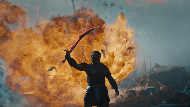 A predator raises his sword before a massive explosion on a rocky planet.