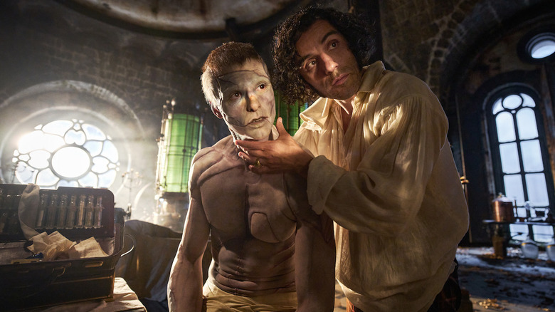 Dr. Frankenstein delicately clasps the Creature's chin as he holds his creation's eyes up to the light.