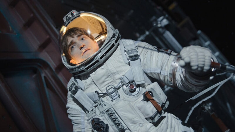 Robert Pattinson stares up at an unseen planet in a space suit.