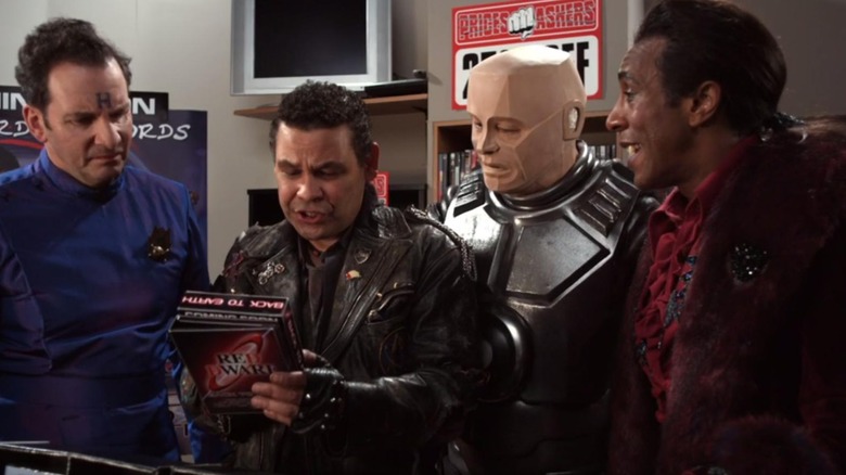 Rimmer (Chris Barrie), Dave Lister (Craig Charles), Kryten (Robert Llewellyn), and Cat (Danny John-Jules) looking at a Red Dwarf box set in "Red Dwarf."