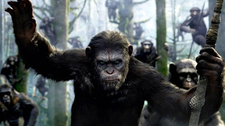 Caesar holding his hand up surrounded by apes in Dawn of the Planet of the Apes