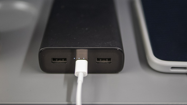 A power bank being charged on a desk next to an iPhone