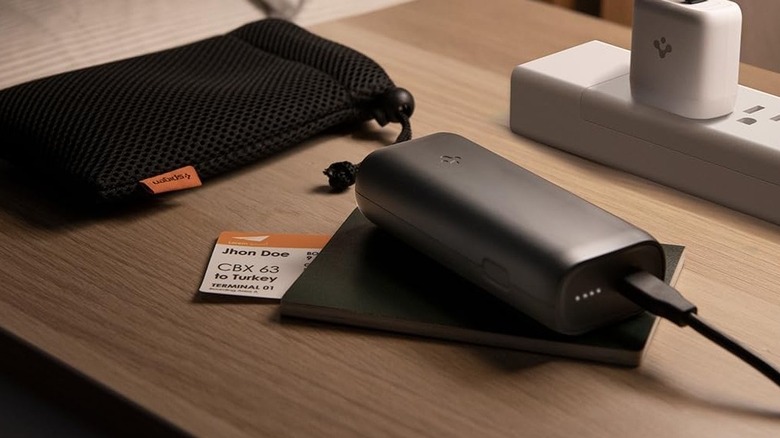 Spigen ArcPack Portable Charger on a desk next to a power strip, passport, and boarding pass