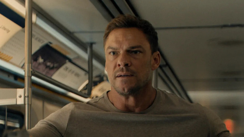Reacher (Alan Ritchson) standing on a bus