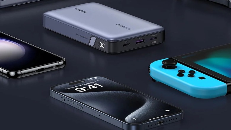 A Ugreen Nexode 100W Power Bank surrounded by multiple gadgets, including an iPhone