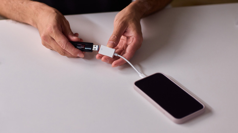 A person connecting a USB flash drive to a phone using an adapter