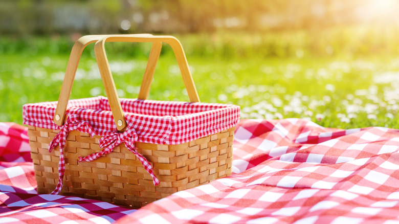 A picnic basket on a checkered blanket in a grassy field.