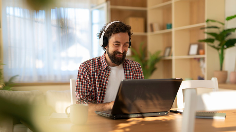 Man wearing headphones and using a laptop in his home office.