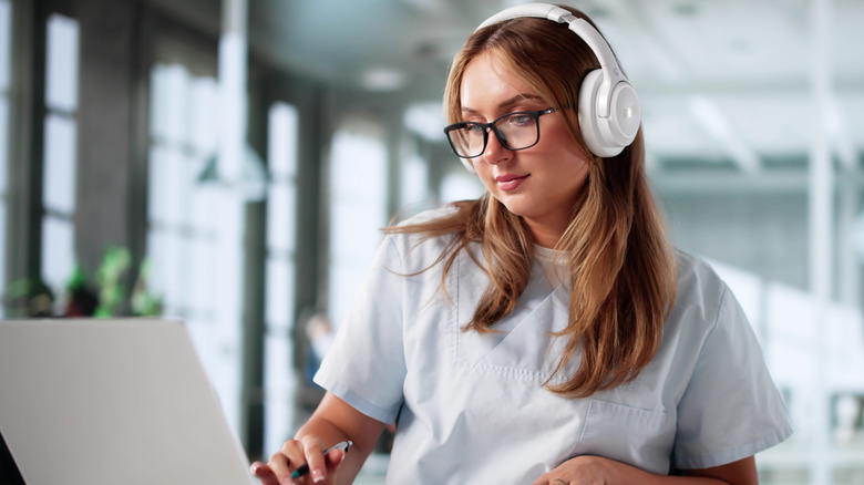 Young woman working on a laptop and wearing headphones in an office setting.