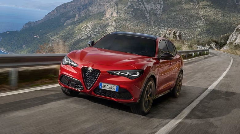 Alfa Romeo Stelvio in red driving on a road with mountains behind.