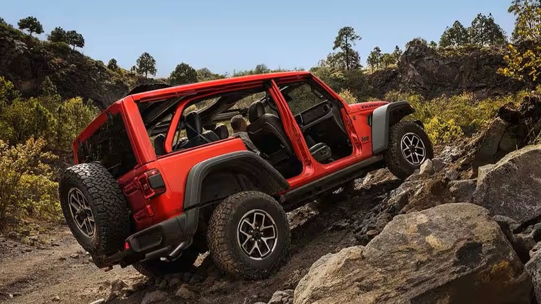 Jeep Wrangler climbing rocks outdoors with open cabin.