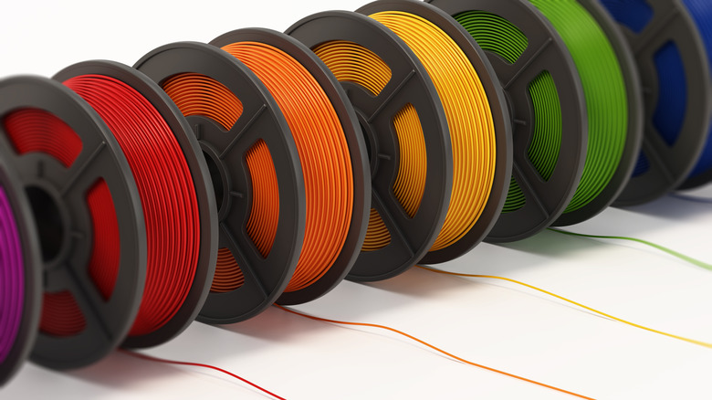Multiple colors of 3D printer filament rolling out on a white background