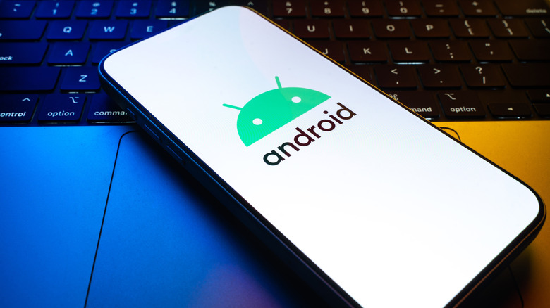 Android smartphone displaying the Android logo on its screen, resting on a backlit laptop keyboard.