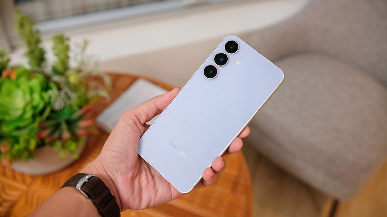 Samsung Galaxy S25 FE held in hand, showing its triple rear camera setup.