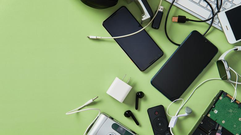 A bunch of electronic gadgets, including a hard drive, phone, camera, headphones, and keyboard on a green background