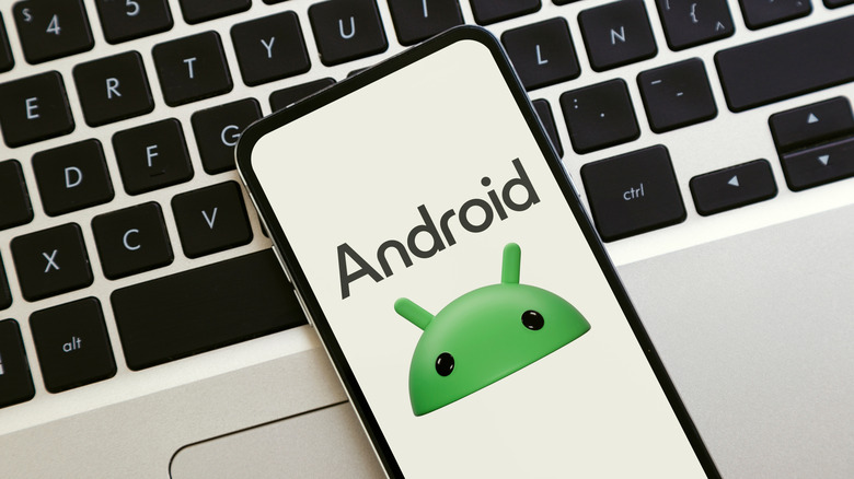 A smartphone displaying the green Android robot logo, placed diagonally on a laptop keyboard.
