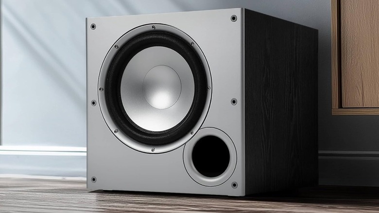 A silver Polk Audio PSW10 subwoofer sitting on a wooden floor, there is a blue wall behind the speaker