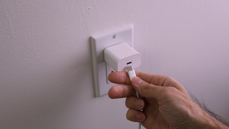A hand connecting a USB-C cable to a power adapter plugged into an outlet