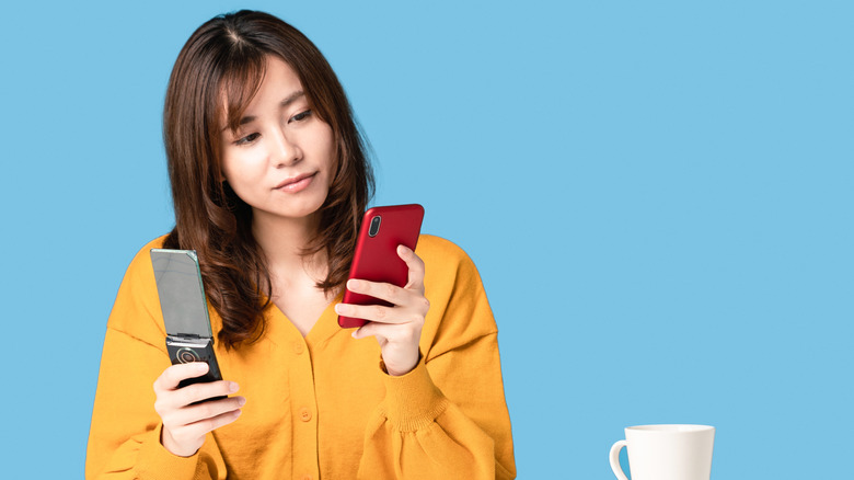 A person holding an older flip phone in one hand a a modern smartphone in the other