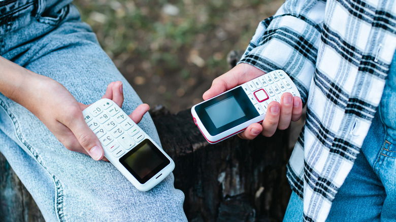 Two people holding white feature phone
