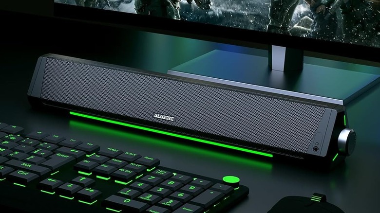 A black Bluedee sound bar next to a keyboard with green lighting