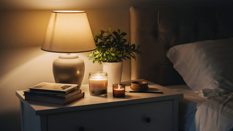 A lamp and candles lit on a bedside table.