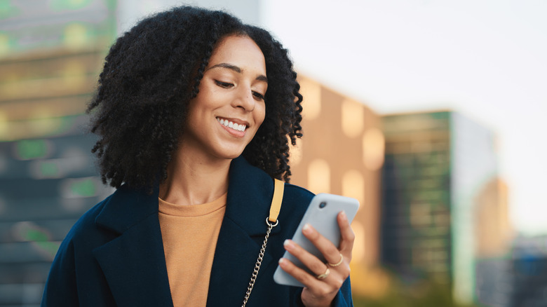 A woman smiling while looking at her smartphone.